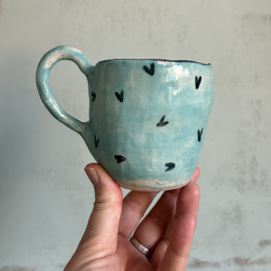 Taza artesanal de cerámica azul agua con pequeños corazones negros pintados a mano.